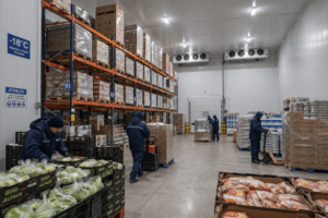 Trabalho em câmara fria de supermercado com caixas organizadas e névoa de congelamento.
